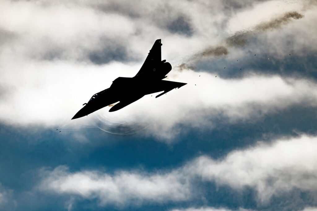 Passage d’un Mirage 2000-5 de l’escadron de chasse 1/2 « Cigognes ». Effet rarissime, sur la photo apparaissent l’effet des ondes de choc derrière les obus ainsi que l’effet des ondes acoustiques circulaires sous l’avion dues à la détonation des canons. Photo non truquée.